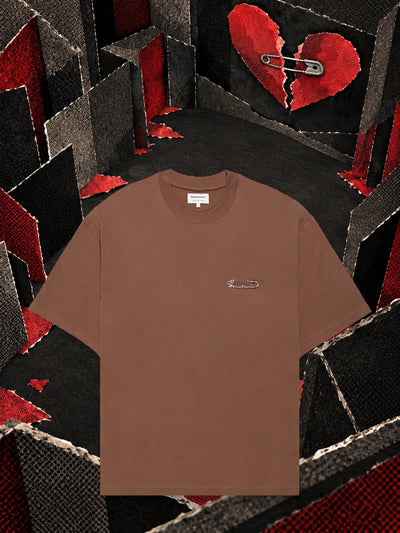 Het bruine T-shirt Brokenheart in een kamer van donker papier, onder een hart van rood papier dat in tweeën is gebroken.