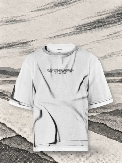 Biały T-shirt Crux nad skrzyżowaniem ścieżek z białego papieru, z długimi smugami szarego węgla niesionymi przez wiatr.