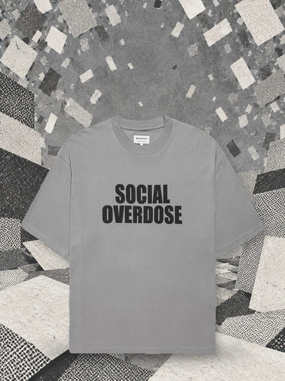 Szary T-shirt Social Overdose pod śnieżycą małych białych i szarych kartoników, nad krajobrazem z papierowych bloków.