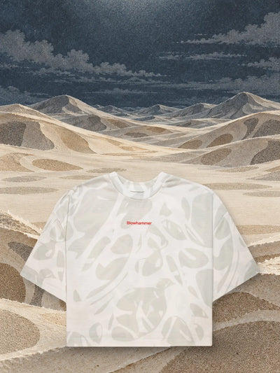 A rövid elefántcsontszínű Strand Ivory póló elefántcsont- és homokszínű papírdűnék fölött.