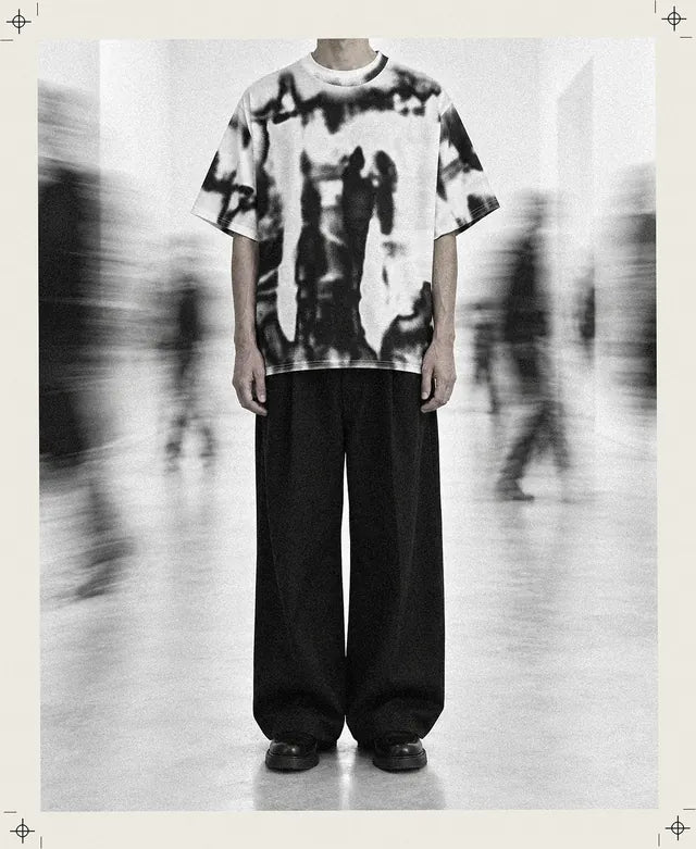 Una persona inventata, ferma e tagliata al collo, indossa la Rift T-Shirt mentre intorno gli altri passano sfocati.